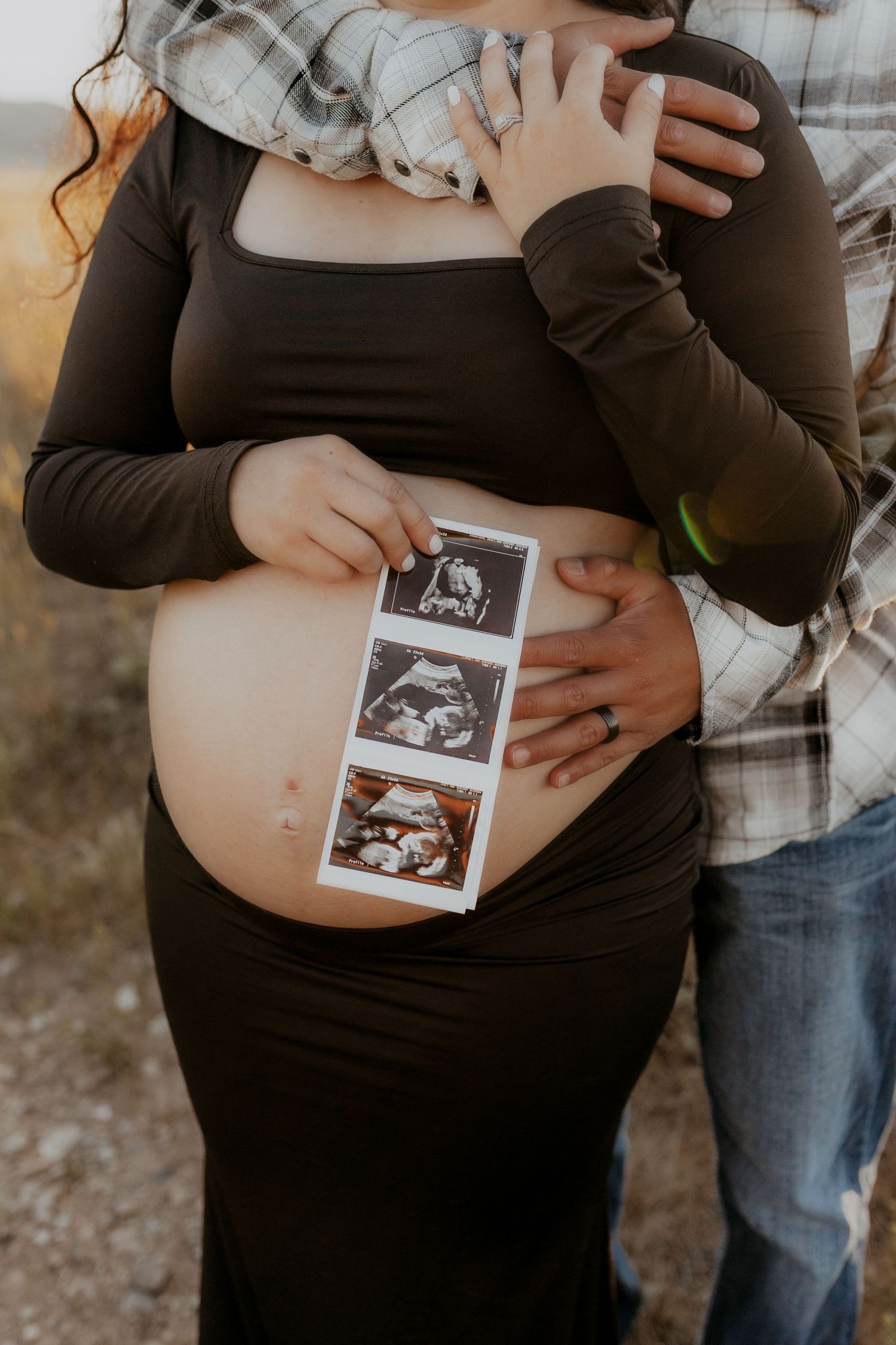 Close-up of ultrasound photos placed on a pregnant belly with caring hands.