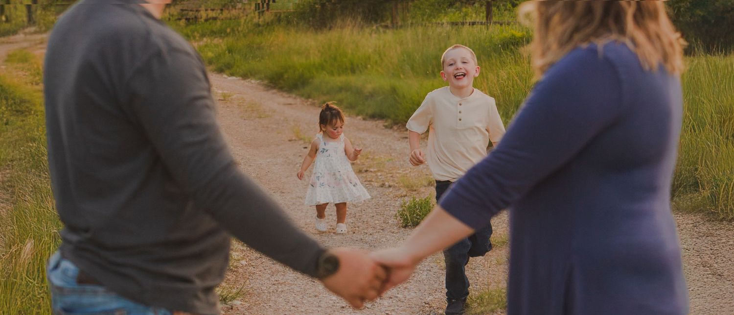 Family holding hands walking on dirt path during sunset.