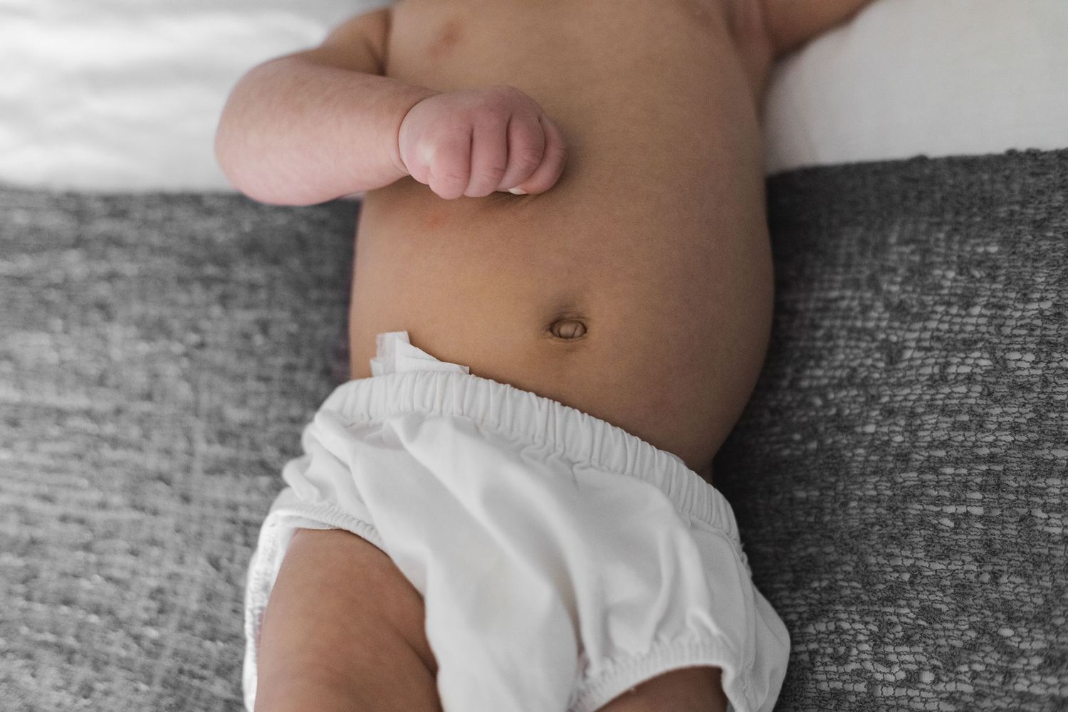 Closeup view showing bare baby feet and legs in soft focus against white cotton fabric and bedding materials.