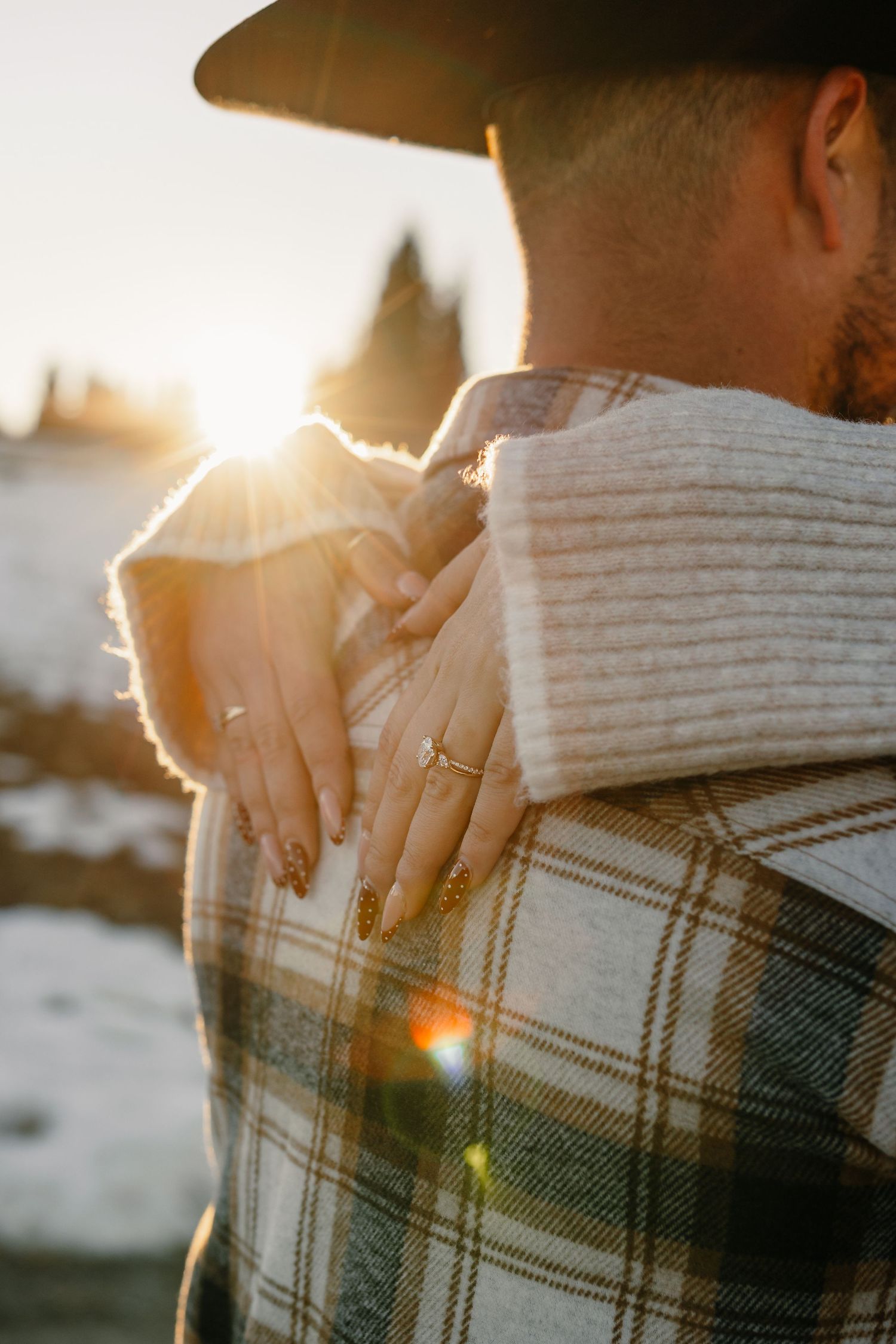 A couple holds hands at sunset with a cozy knit sweater and plaid blanket visible in warm golden light.
