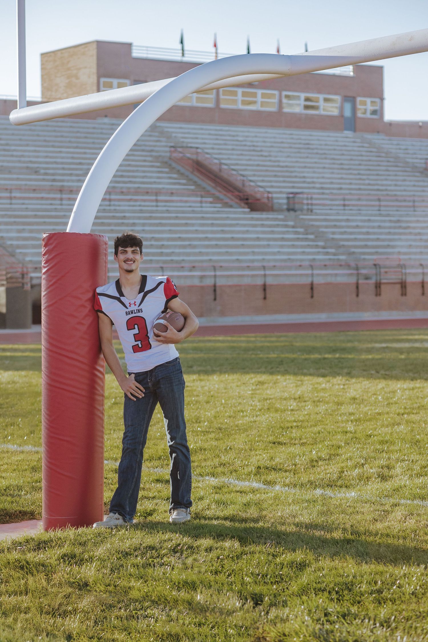 Football player posing next to goal post on sports field wearing jersey number 3.