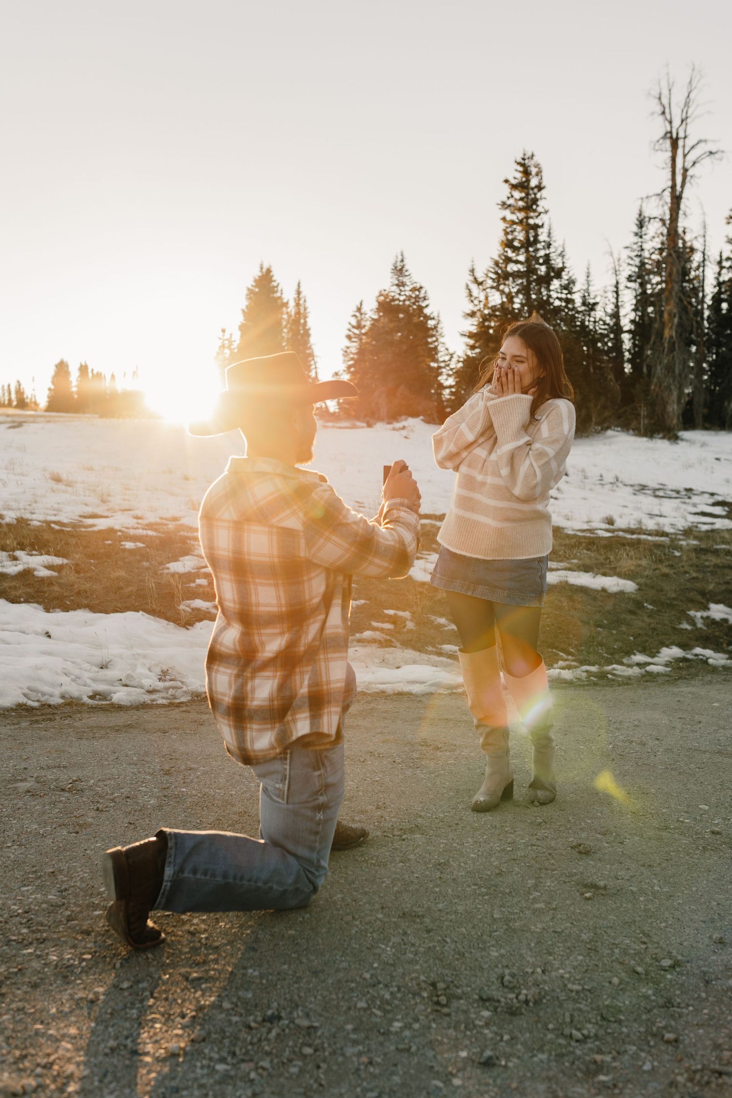 Couple enjoying a romantic sunset moment in a snowy mountain landscape with evergreen trees in the background.