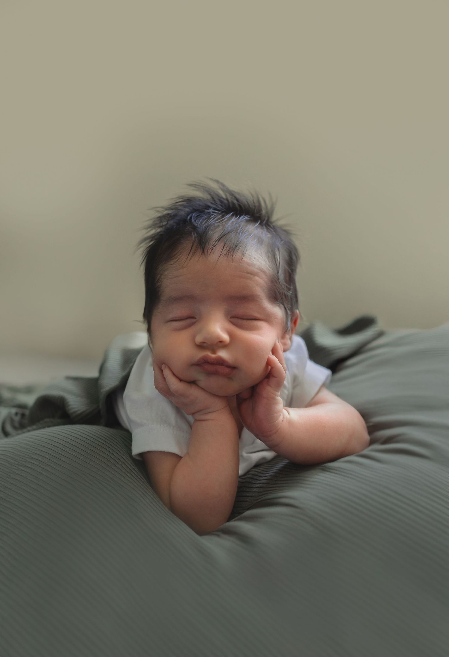 A baby sleeps peacefully on soft bedding with eyes closed and hands tucked under their cheeks.