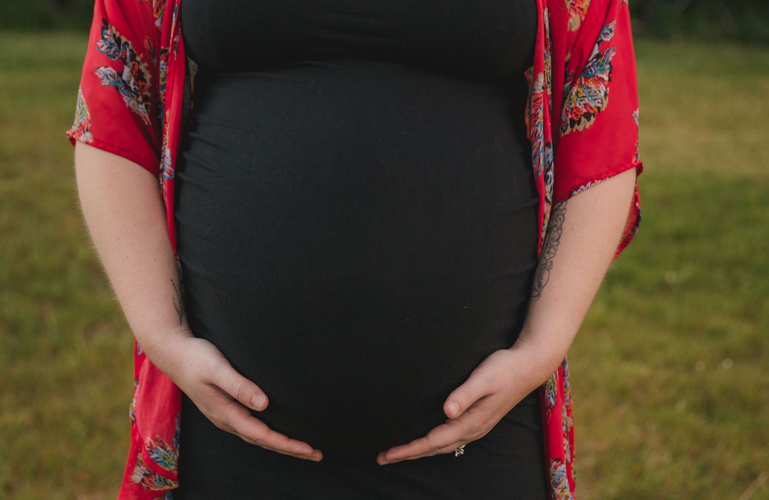Close-up view of a pregnant belly with hands cradling the bump, wearing a red floral overlay.