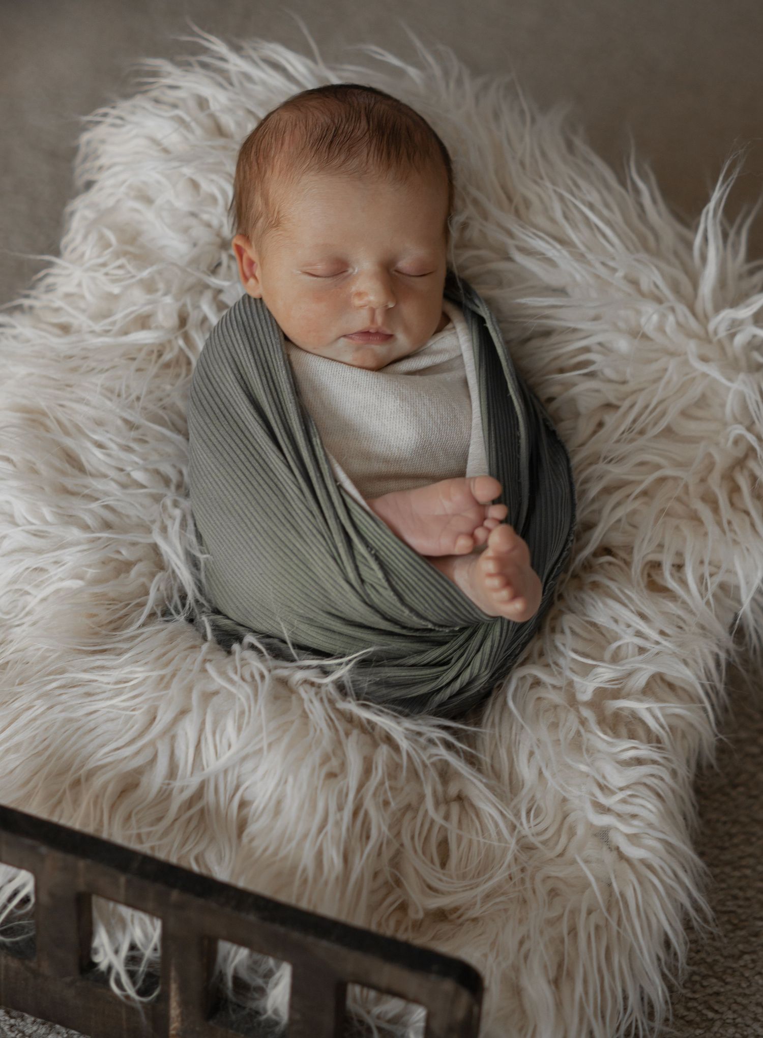 A newborn sleeps peacefully while wrapped in a soft gray swaddle on a fluffy white fur blanket from multiple angles.