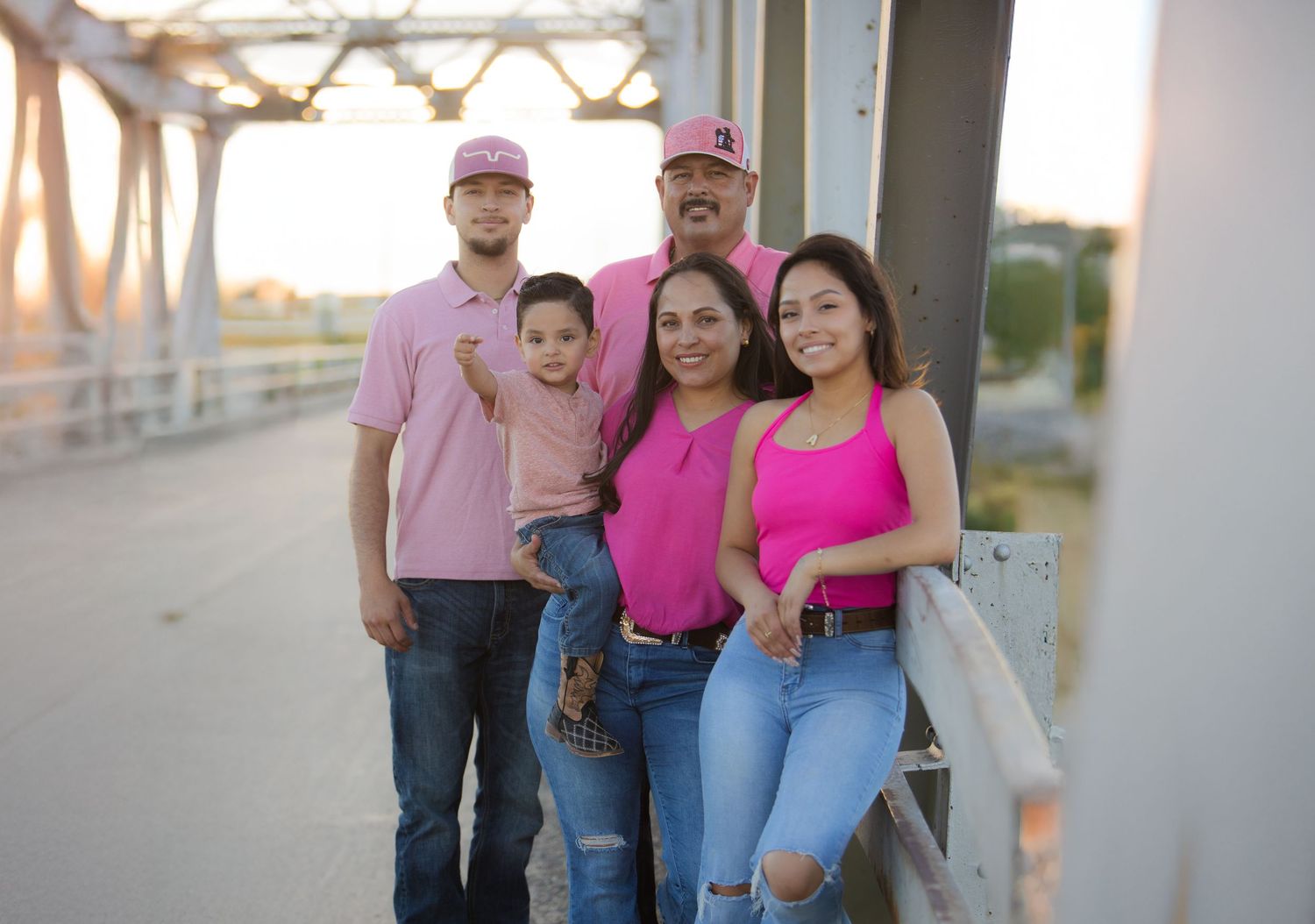 A group in pink and casual attire poses together on a metal walkway at sunset.