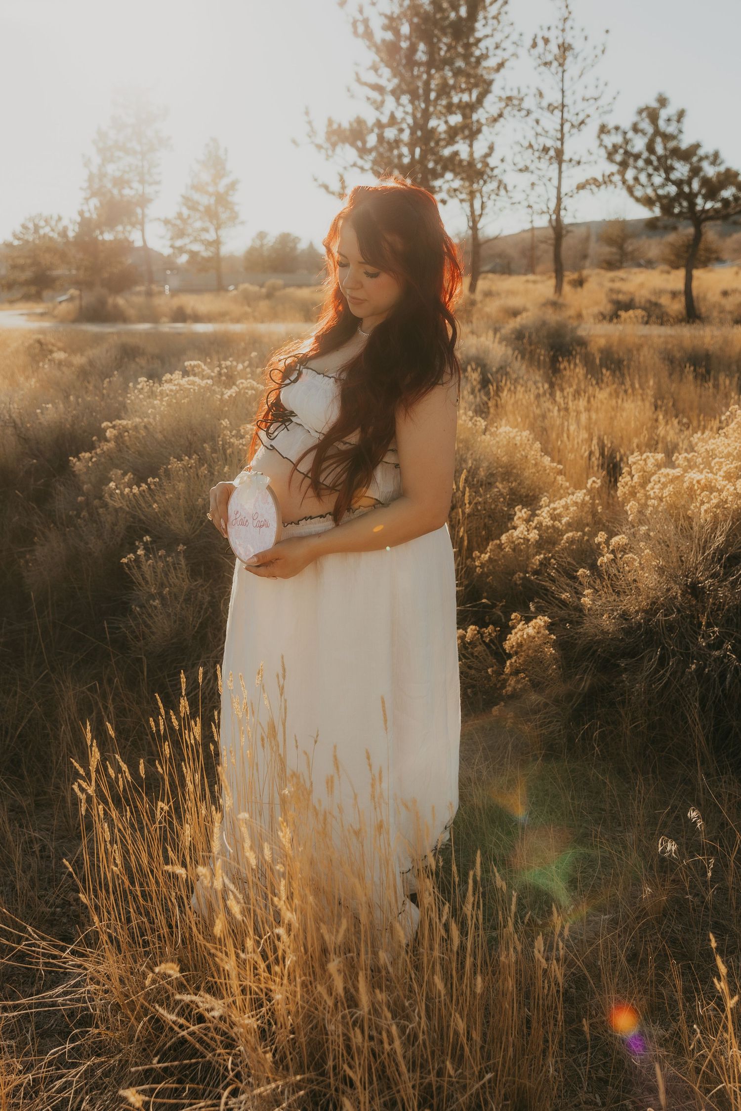A figure in a flowing white dress stands among golden sunlit grasses during sunset creating a dreamy outdoor scene.