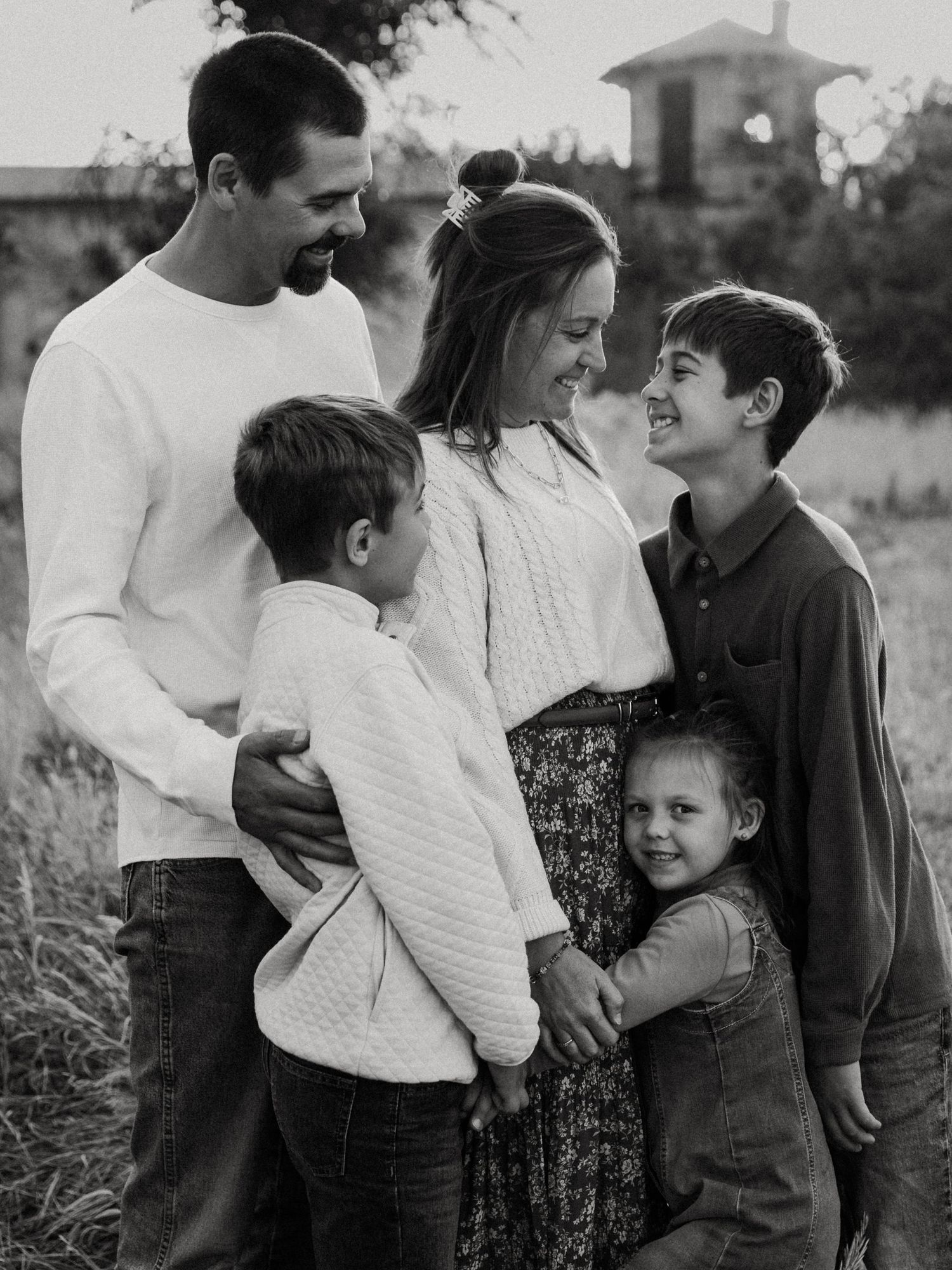 Black and white family portrait of parents with three children embracing outdoors in a field at dusk.