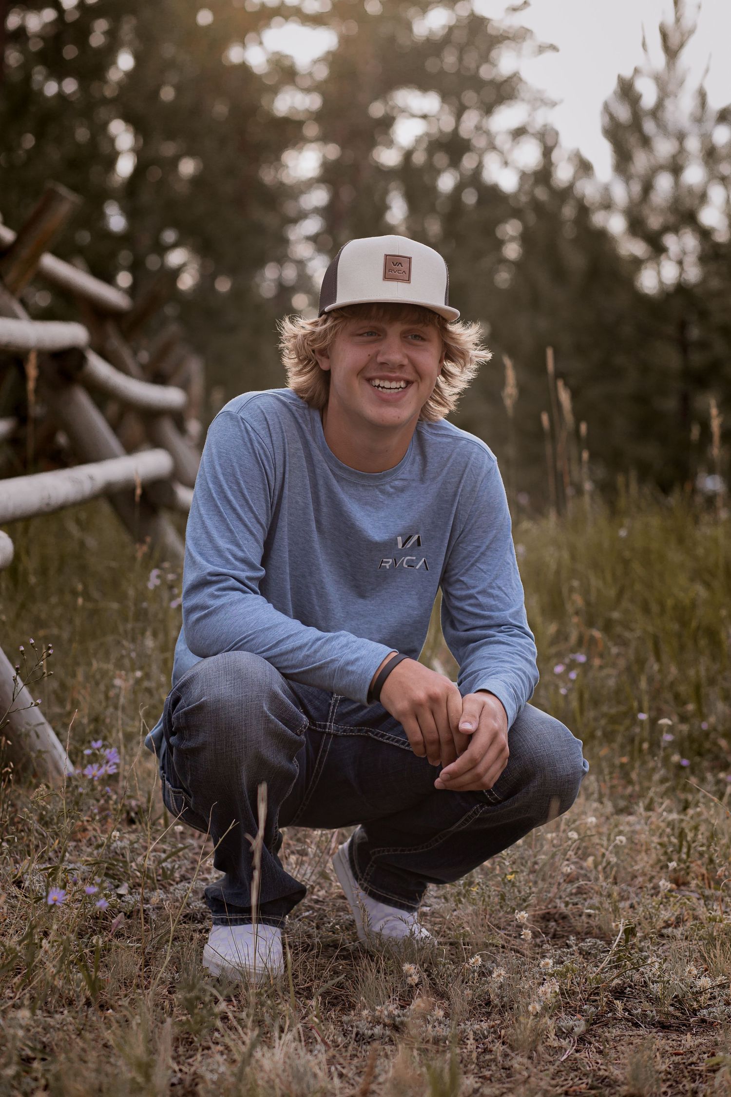 Person in grey sweatshirt and baseball cap crouching in outdoor setting.