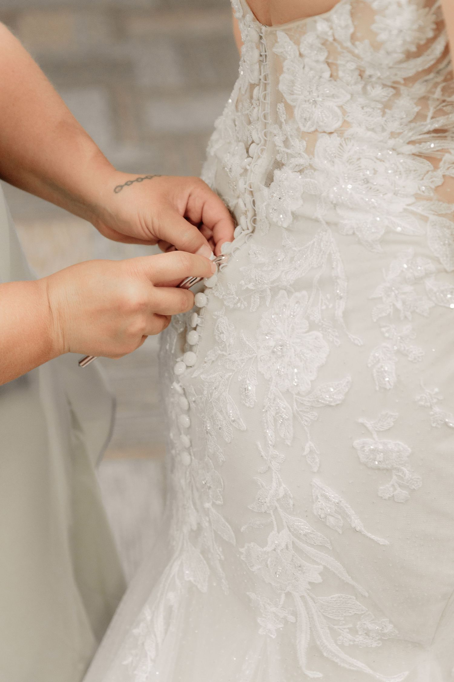 Close-up view of hands adjusting the back buttons and delicate lace details on an elegant white wedding dress.