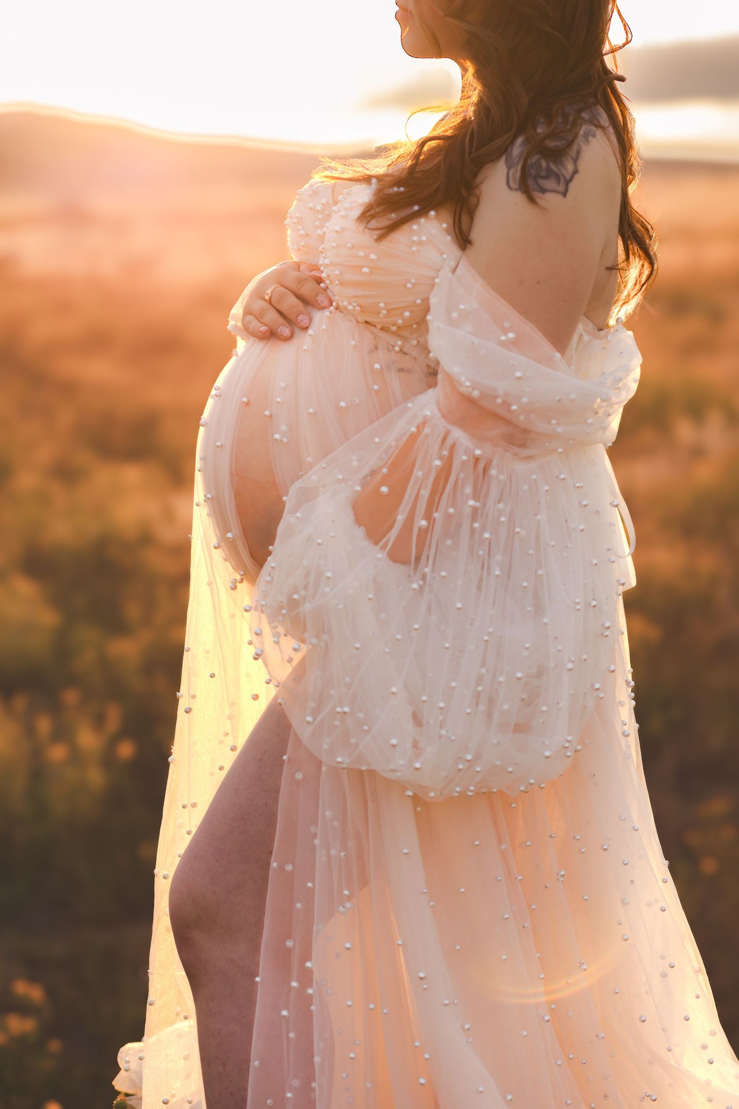 A maternity photo in a flowing white dress during golden hour sunset.