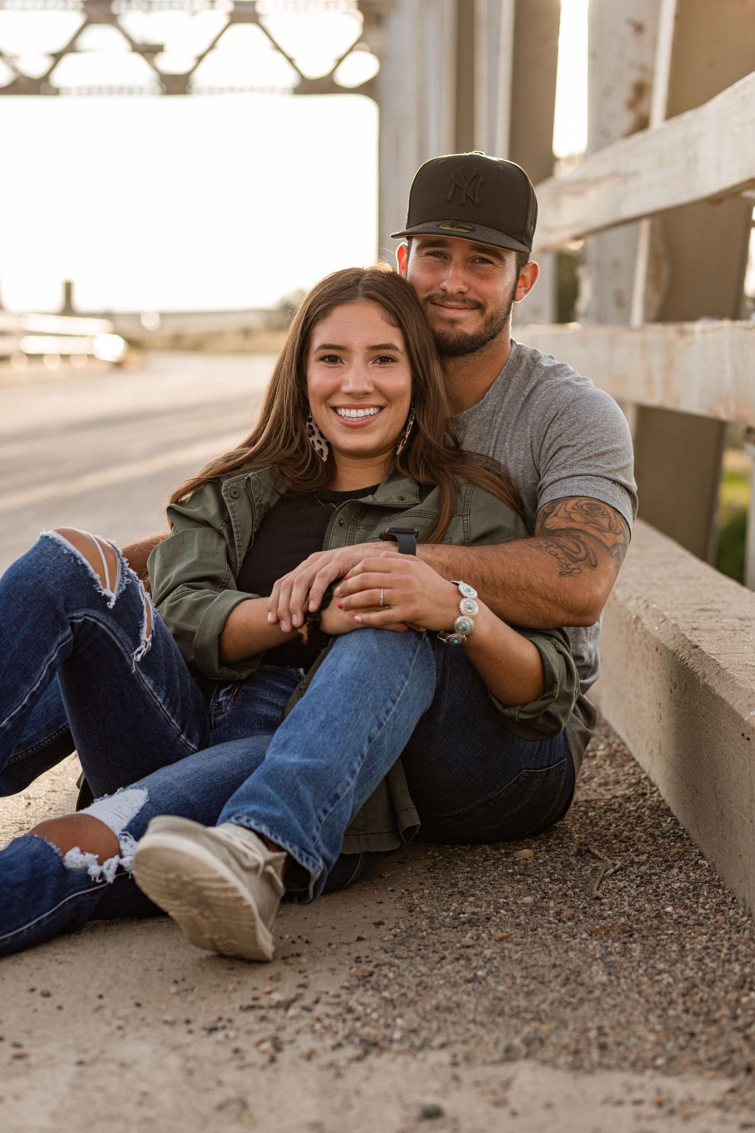 A couple lies together on a paved surface during a casual outdoor photo session.