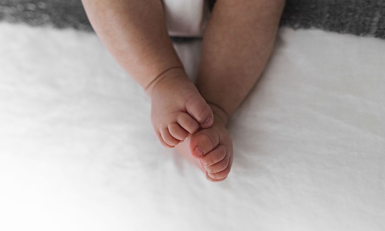 Tiny baby feet casting shadows on a white blanket in soft natural light.