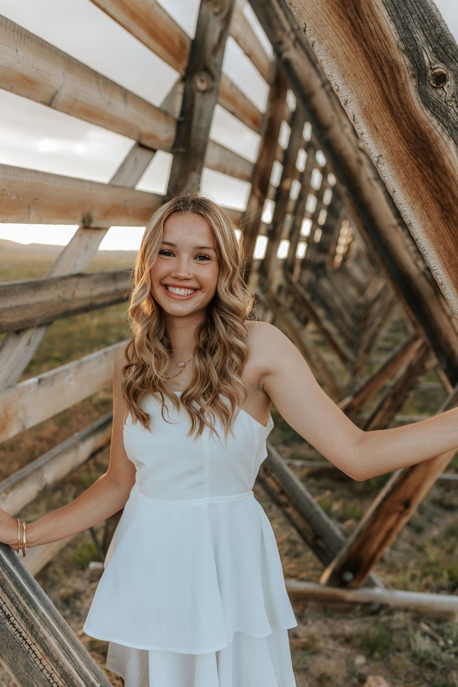 A person in a white flowing dress poses on a rustic wooden bridge structure in warm natural lighting.