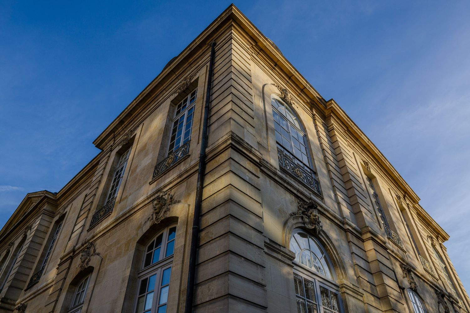 Low angle view of a historic yellow building facade with ornate windows against blue sky.