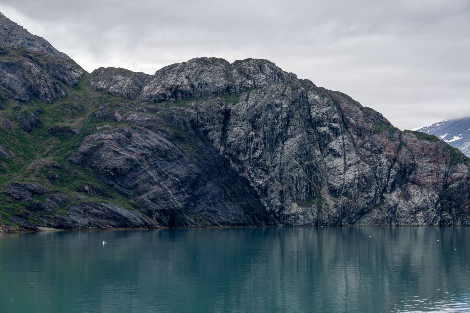 Rugged rocky cliffs rise dramatically from the turquoise waters of an Alaskan fjord.