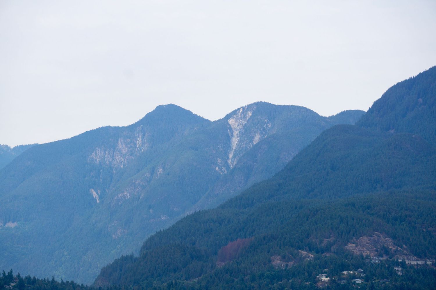 Majestic forested mountains rise into misty skies with layered peaks fading into the distance.