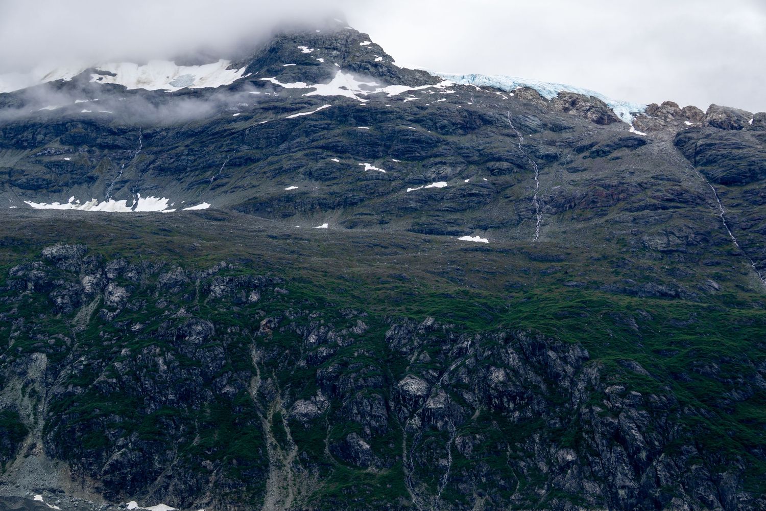 Misty mountain peaks rise above rocky cliffs with patches of snow visible through low clouds.