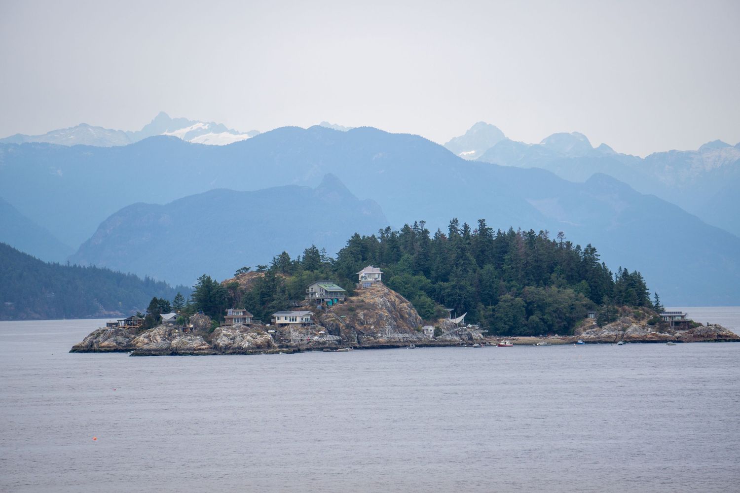 A small rocky island covered in trees rises from misty waters with mountain peaks in the distance.