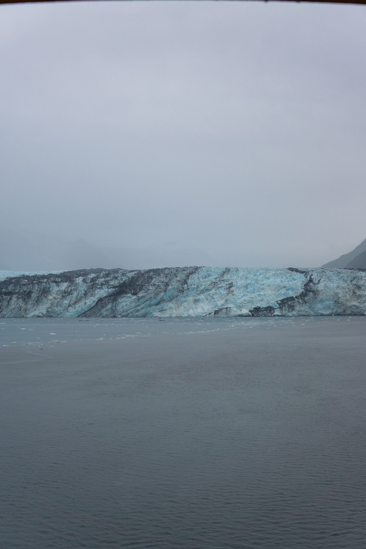 Stark white and blue glacier terminus stretches across gray waters under moody skies.