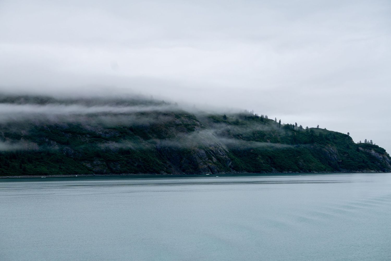 Misty mountain coastline with low-hanging fog over dark waters on a moody day.