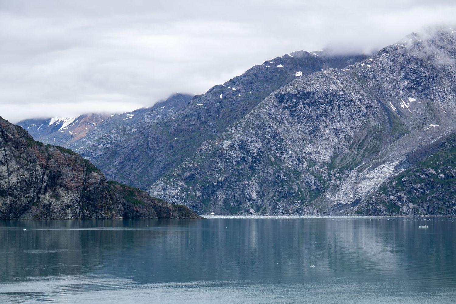 Dramatic mountain cliffs reflect in the pristine turquoise waters of a glacial fjord.
