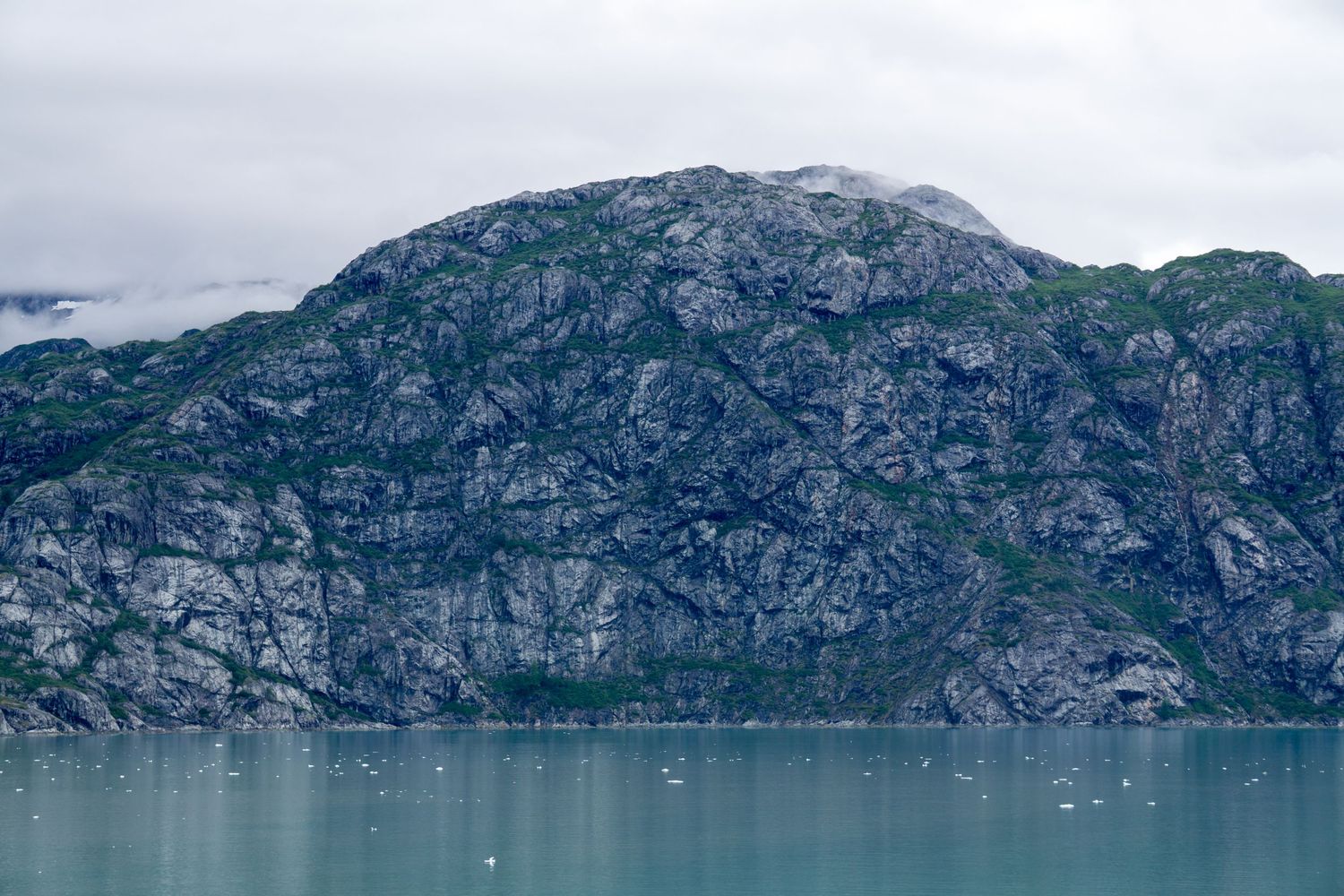 Steep rocky cliffs meet pristine turquoise waters in a dramatic glacial fjord.
