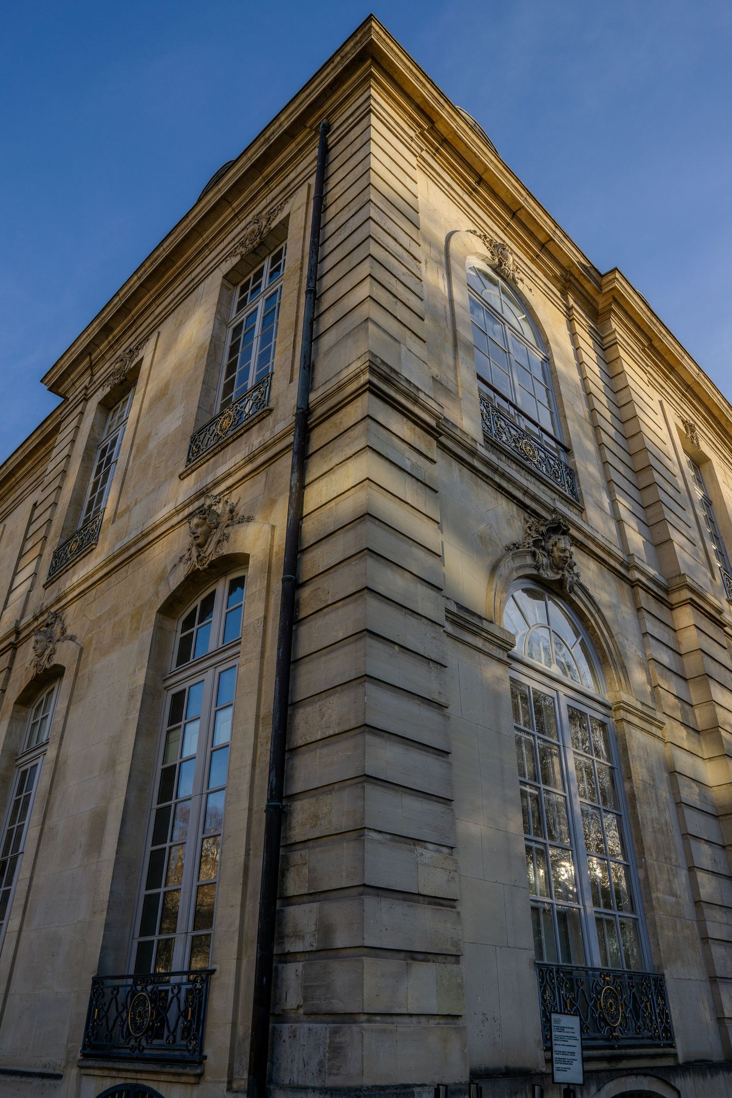 Ornate French building exterior with tall windows, wrought iron balconies and classical architectural details against blue sky.