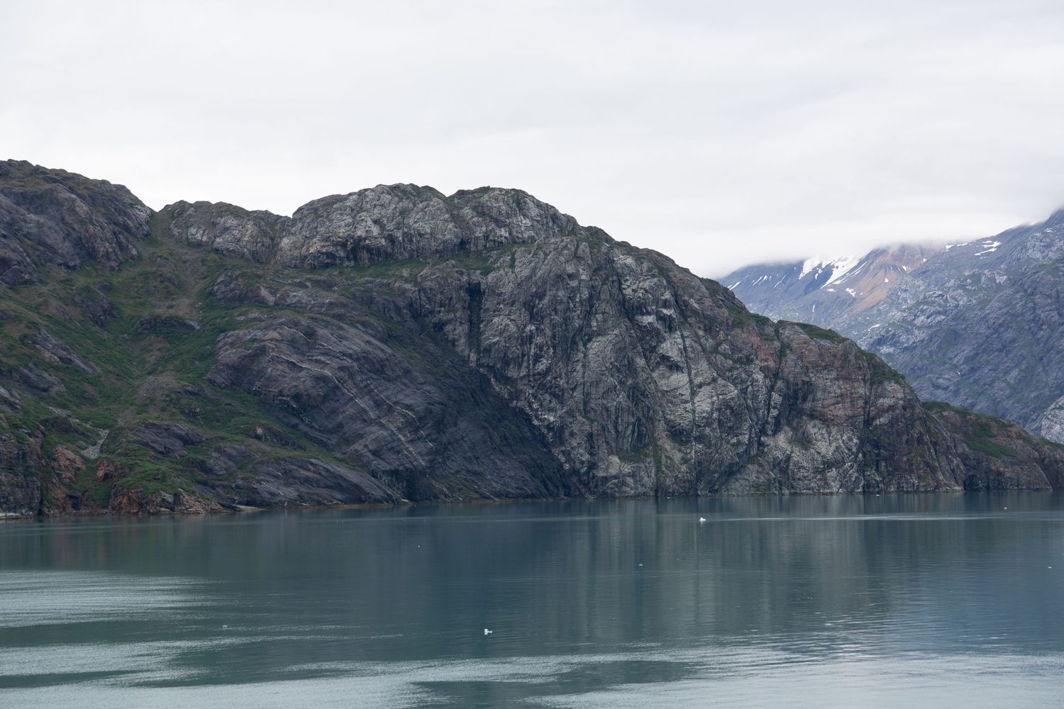 Steep rocky cliffs meet tranquil turquoise waters in a serene glacial bay landscape.