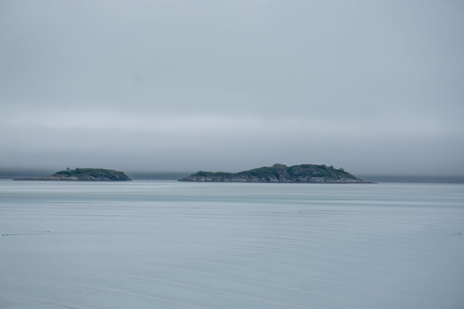 Two small islands emerge from calm gray waters under an overcast sky.