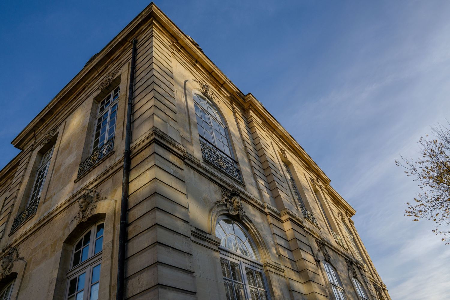 Low angle architectural view of a classical European building facade with tall windows against a blue sky.
