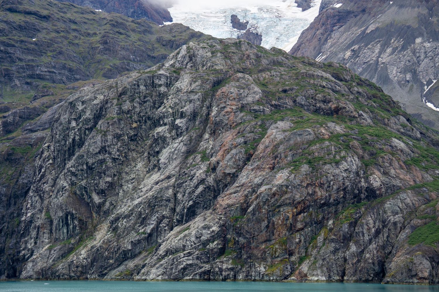 Rugged rock formations and patches of snow mark the landscape near an Alaskan glacier.