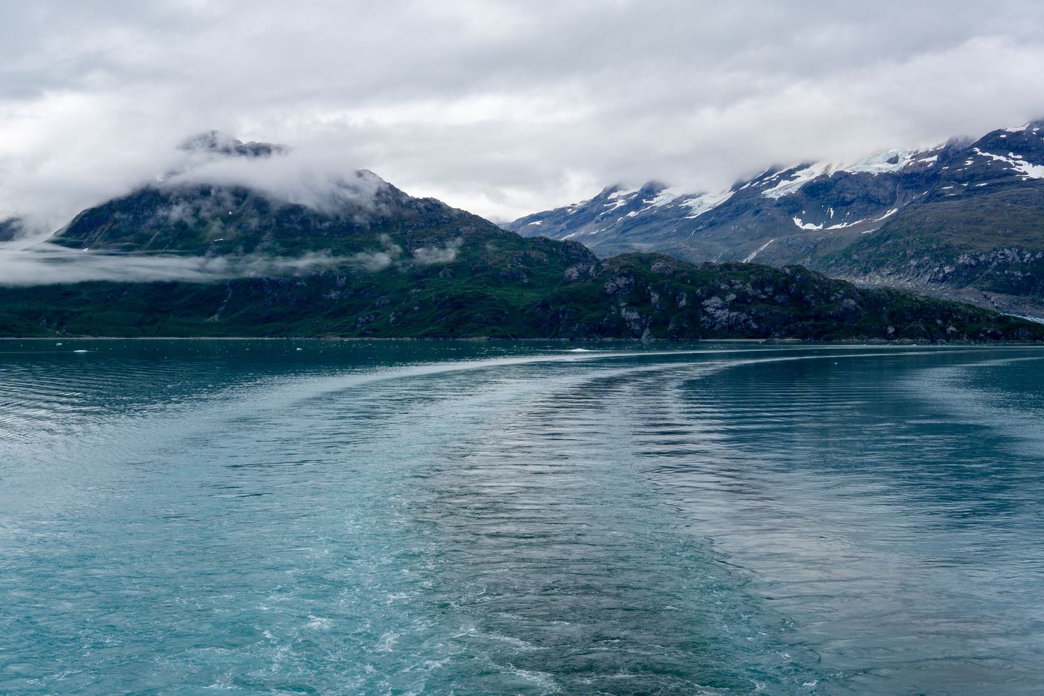 Cloudy mountain landscape reflects in pristine turquoise waters of an Alaskan fjord.