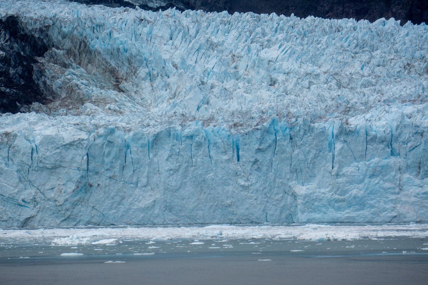 Close-up view of a towering blue glacier wall showing intricate ice formations and crevasses.