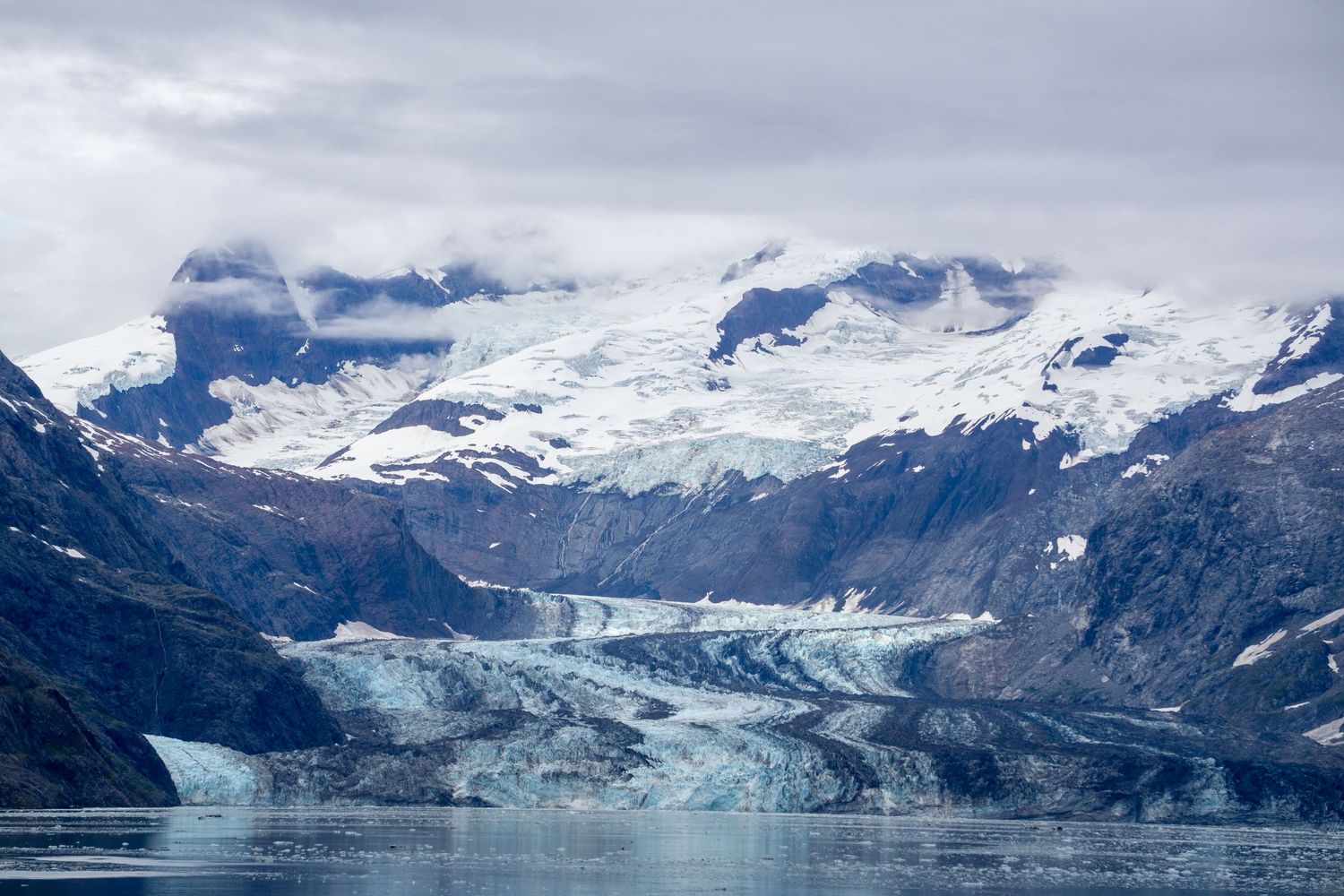 Massive blue glaciers flow between snow-capped mountains into the waters of Glacier Bay, Alaska.