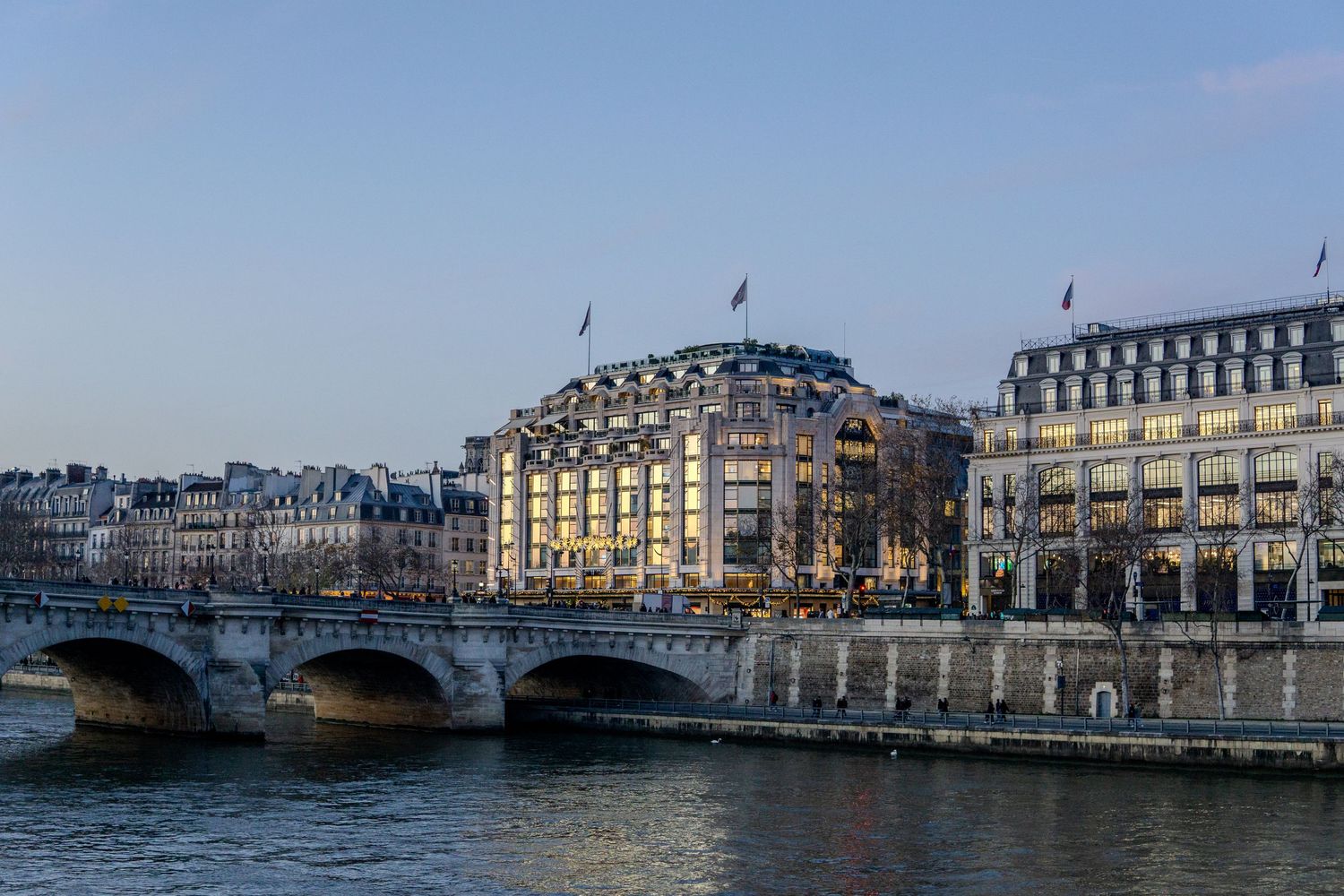 View of the iconic Seine River bridge and elegant hotels in Paris at dusk with white stone buildings and blue sky.