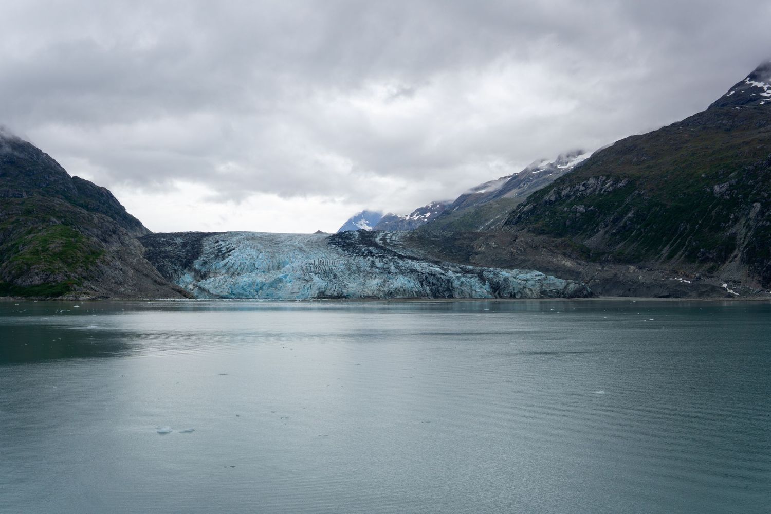 Glacial ice field stretches between mountains reflecting in the still waters of an Alaskan bay.