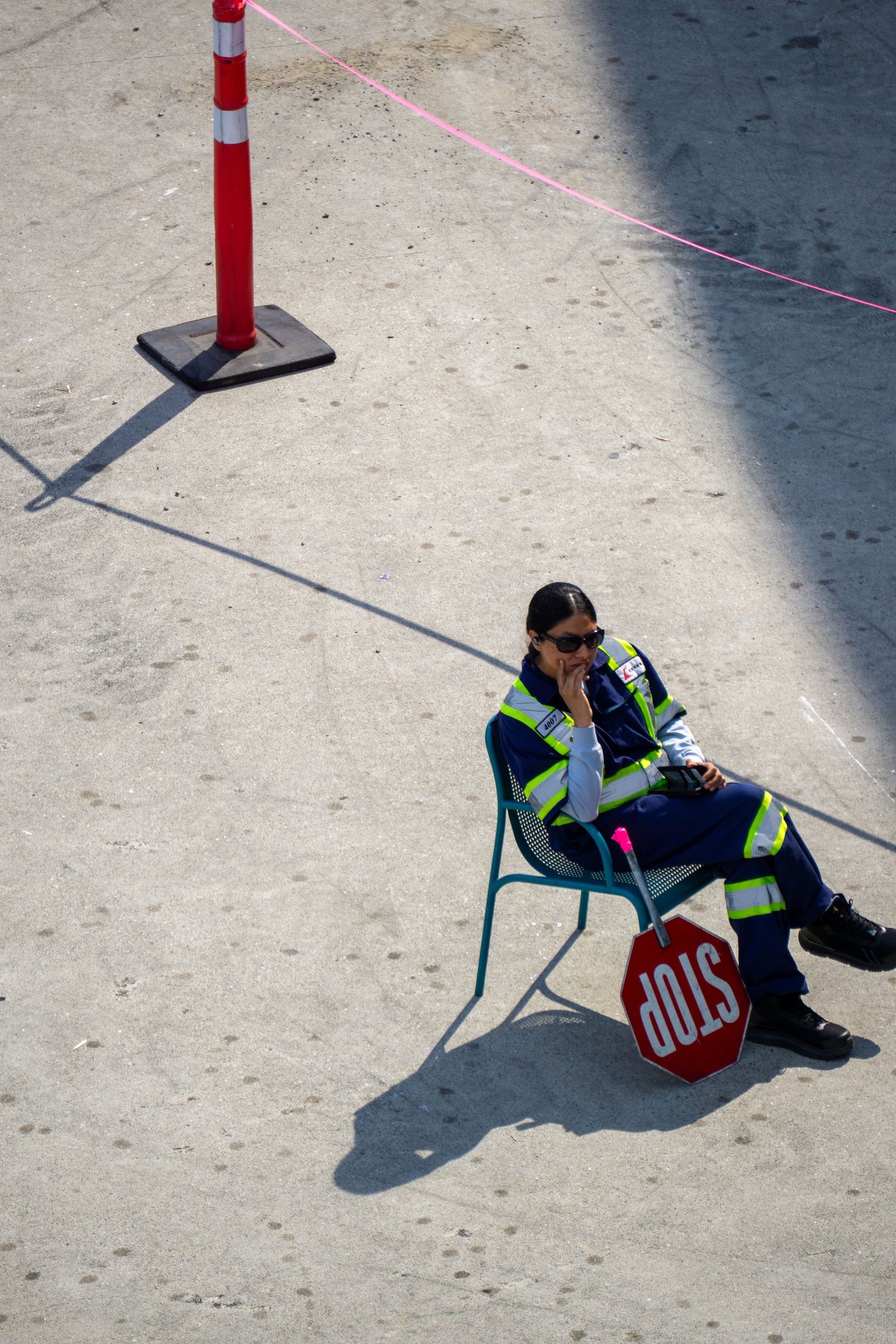 Security guard in high-visibility vest sitting on chair next to traffic bollard.