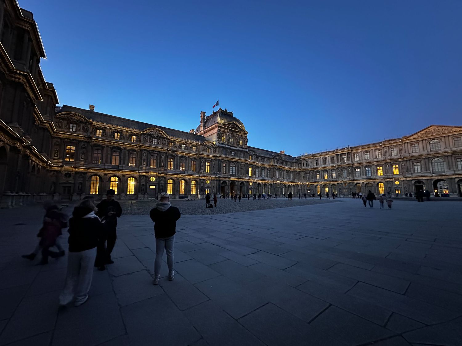 Evening view of the illuminated courtyard at the Louvre Museum in Paris with its iconic architecture against a deep blue sky.