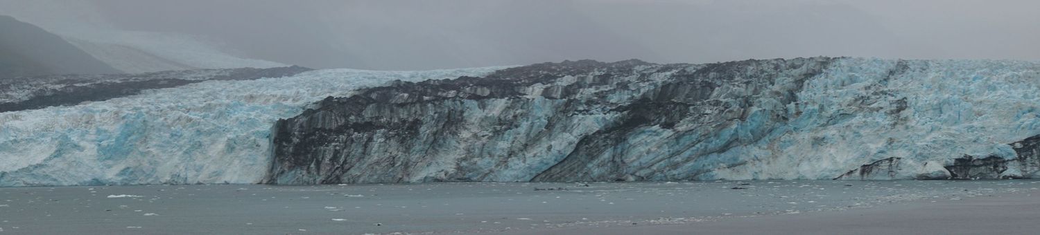 Wide panoramic view of a glacial wall with blue ice formations along the coastline.