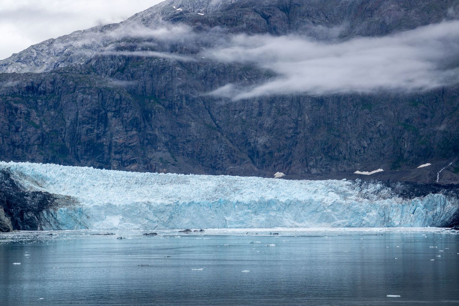 Blue glacial ice face stretches across the water between steep mountain walls.