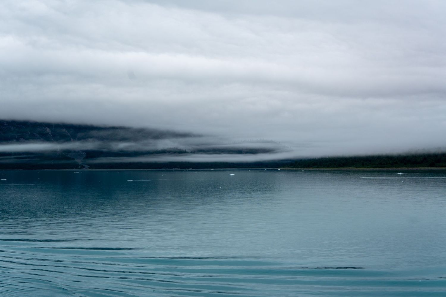 Ethereal fog blankets distant shoreline over calm turquoise waters in minimalist seascape.