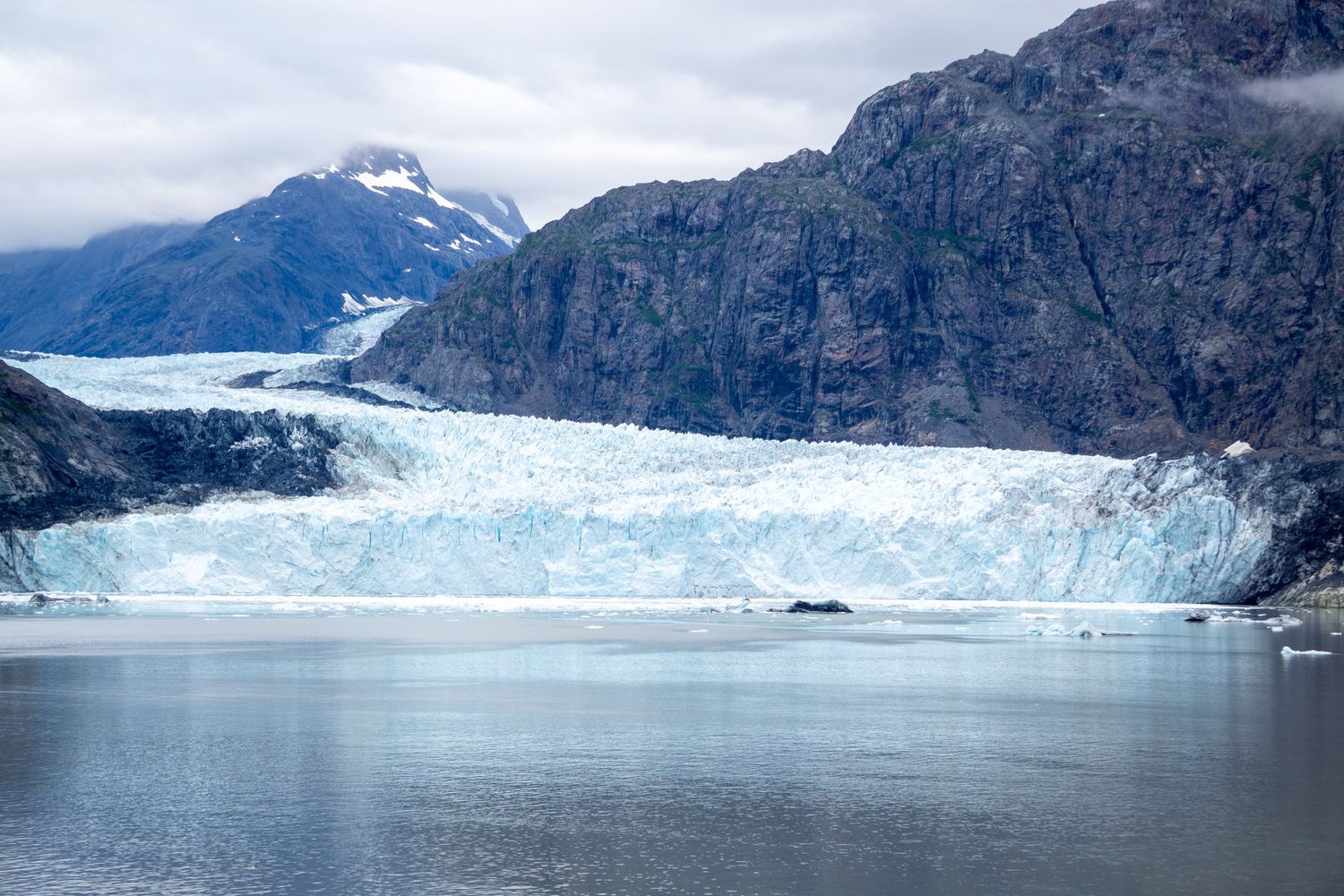 Tidewater glacier with distinctive blue ice flows between mountain peaks into ocean waters.
