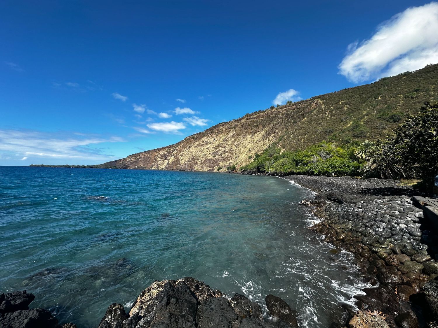 Scenic coastal view of a rocky beach with turquoise water and steep cliffs under blue skies.