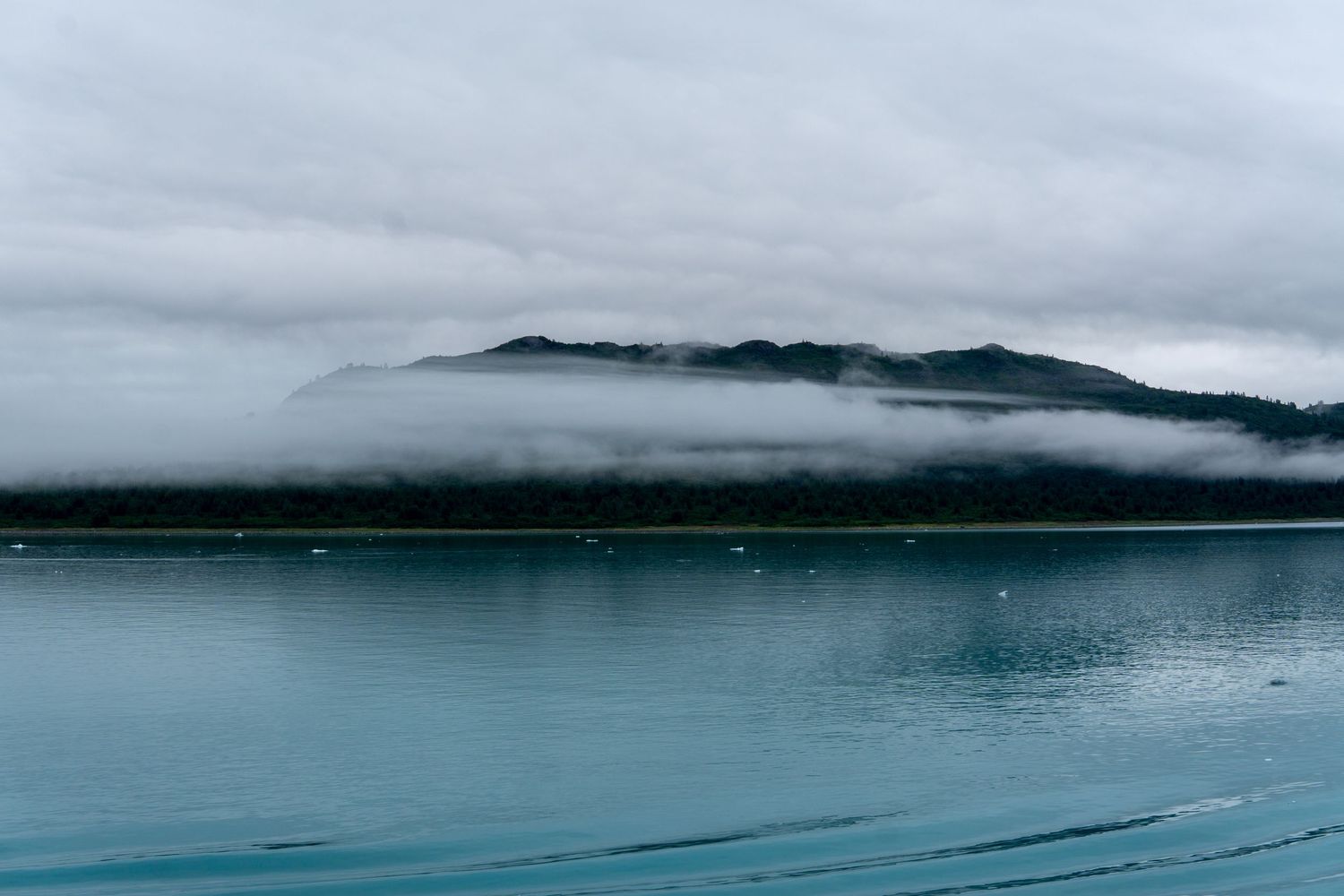 Low-lying clouds wrap around coastal mountains above serene turquoise waters.