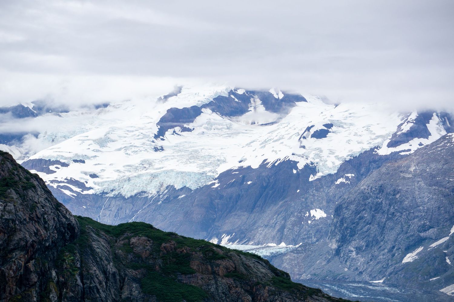Snow-covered mountain peaks and glaciers tower above the rugged Alaskan landscape.
