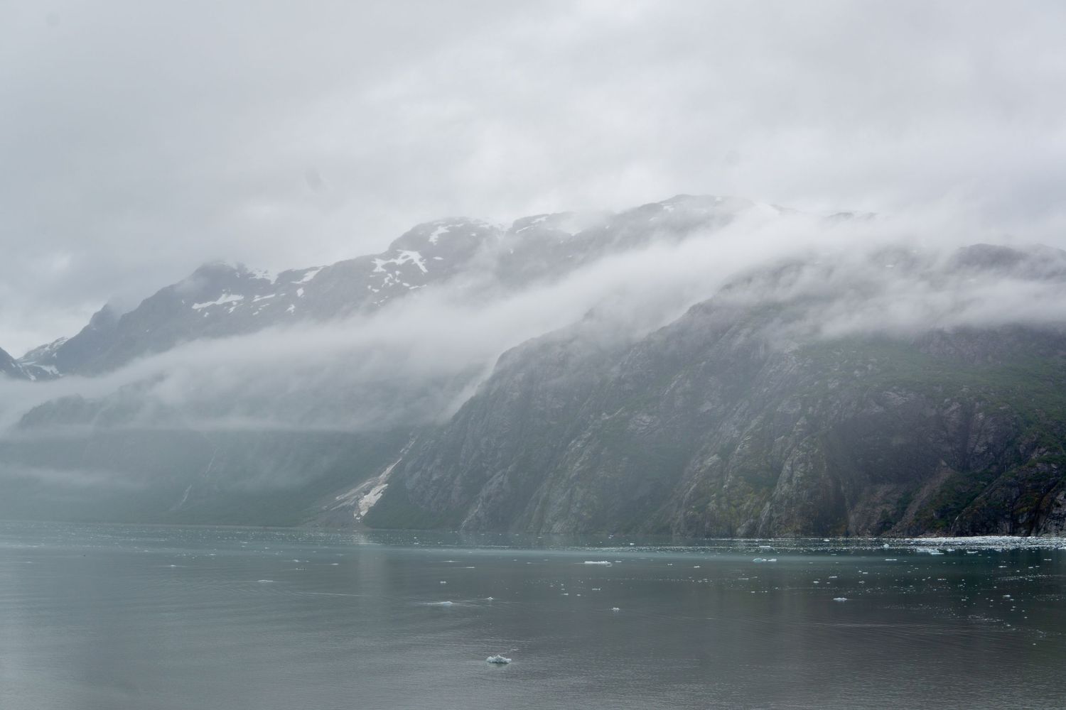 Misty mountains rise dramatically from a tranquil fjord in Alaska's glacial landscape.