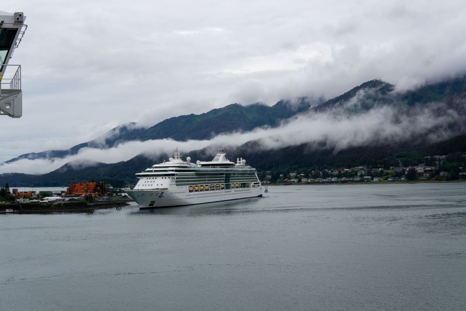 Large cruise ship docked in Alaskan harbor with misty mountains in background.