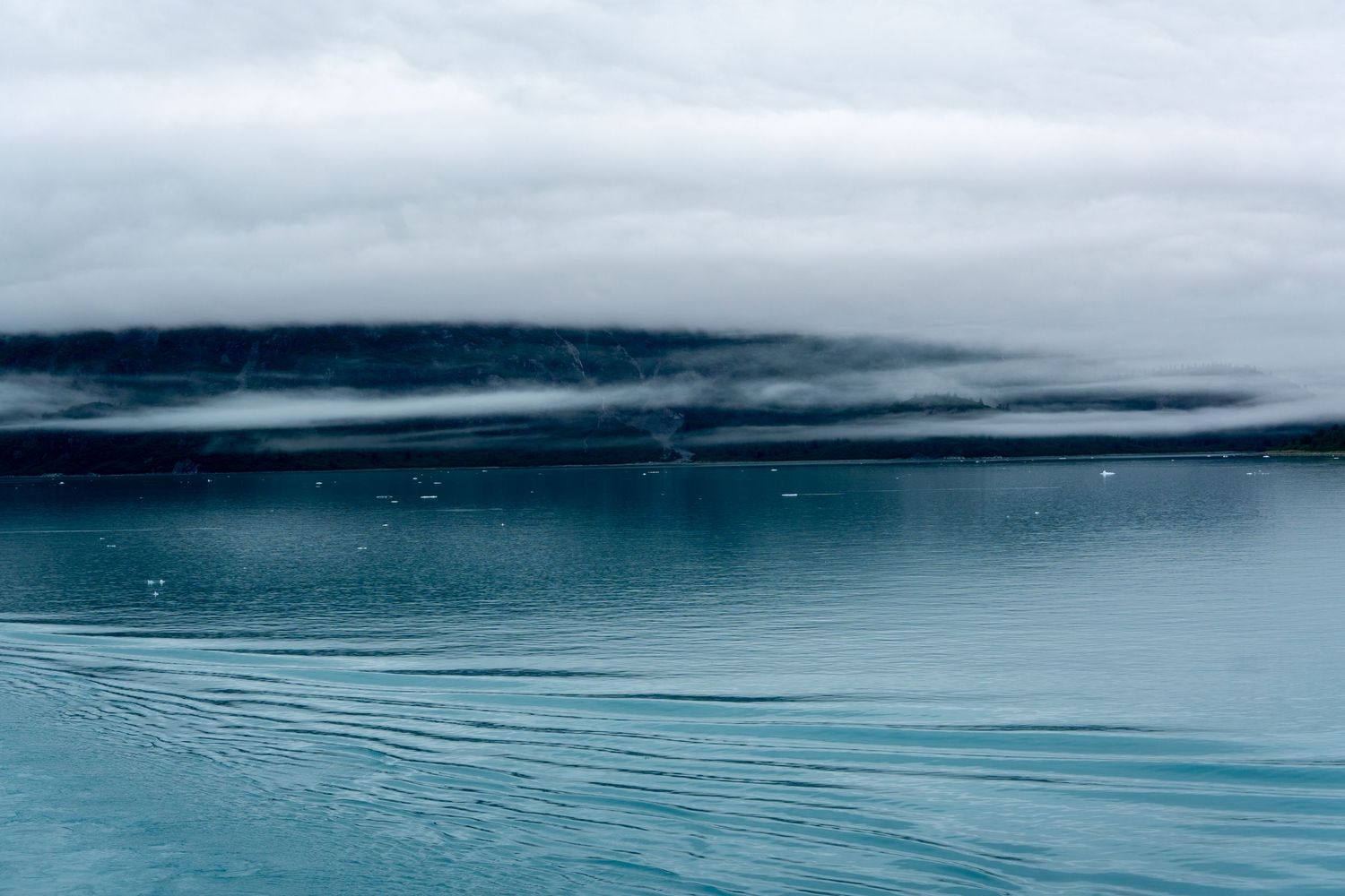 Minimalist seascape with layers of fog hanging over tranquil turquoise waters.