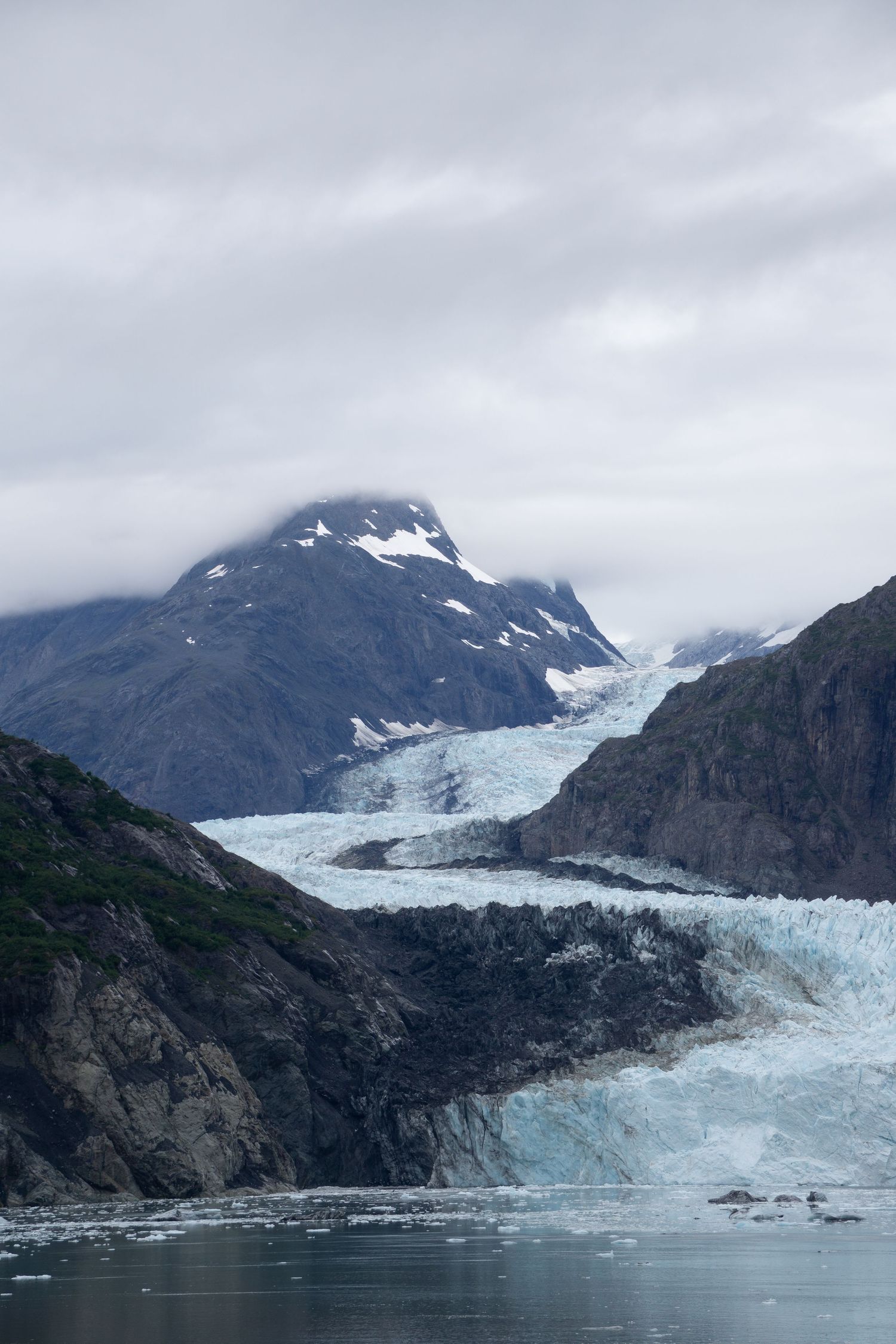 Dramatic glacier cascades down mountain face into misty fjord waters.